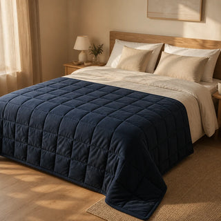 Couverture lestée Somnolia bleu nuit dépliée par-dessus la couette d'un lit en chêne clair