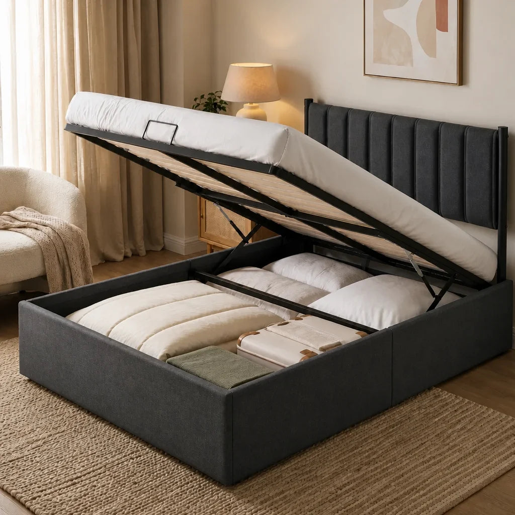 Coffre du lit ouvert sur son vérin hydraulique, révélant couettes, oreillers et valise rangés sous le couchage