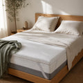 Surmatelas Somnolia posé sur un lit en chêne clair, draps en lin froissé écru et plaid vert sauge