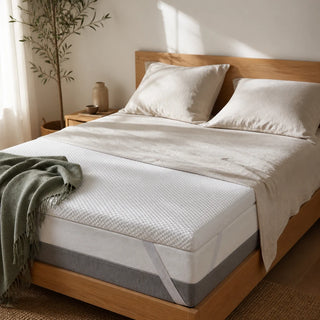 Surmatelas Somnolia posé sur un lit en chêne clair, draps en lin froissé écru et plaid vert sauge